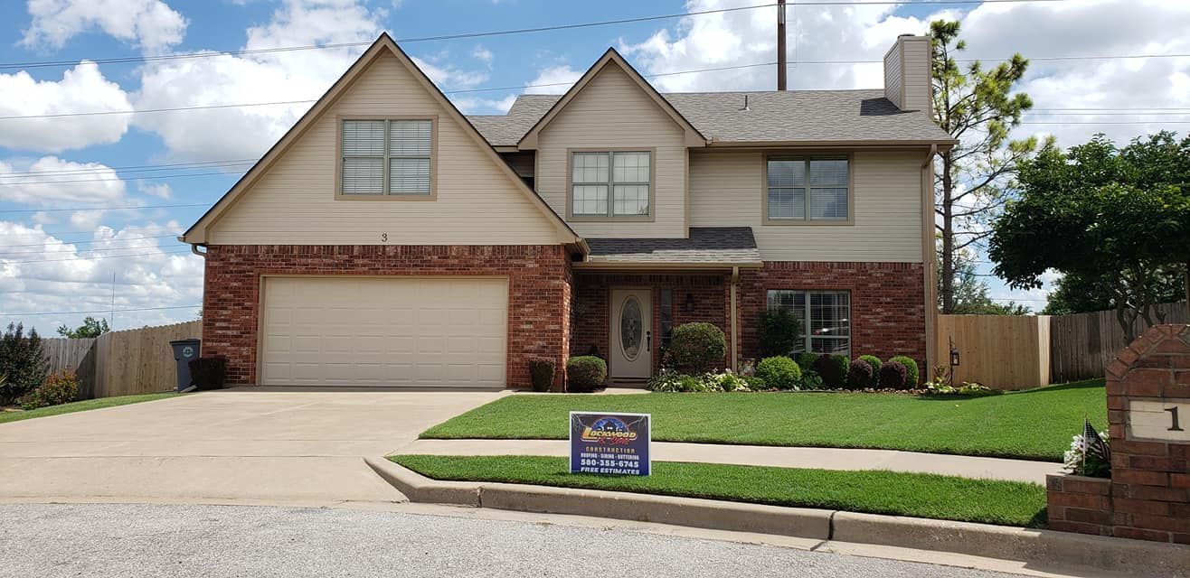 Two-story brick house with a garage, green lawn, blue sky. Sign in front.