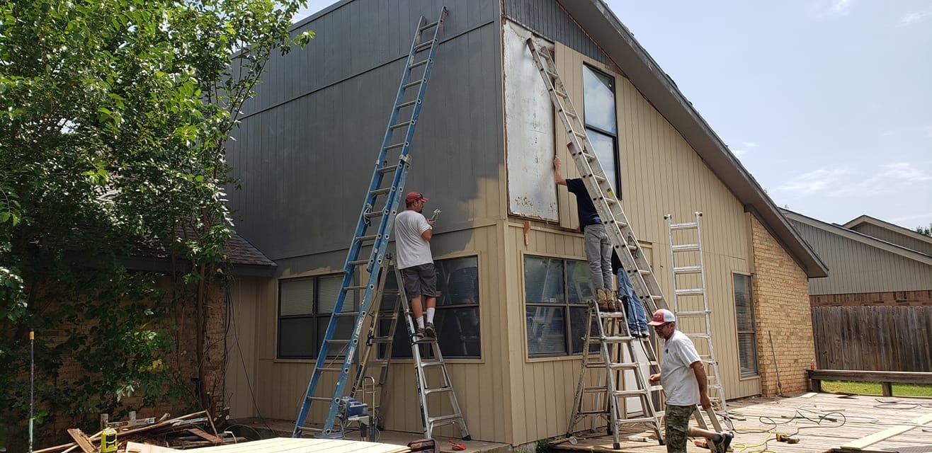 Three men painting the exterior of a house; two on ladders, the house is beige with grey siding.