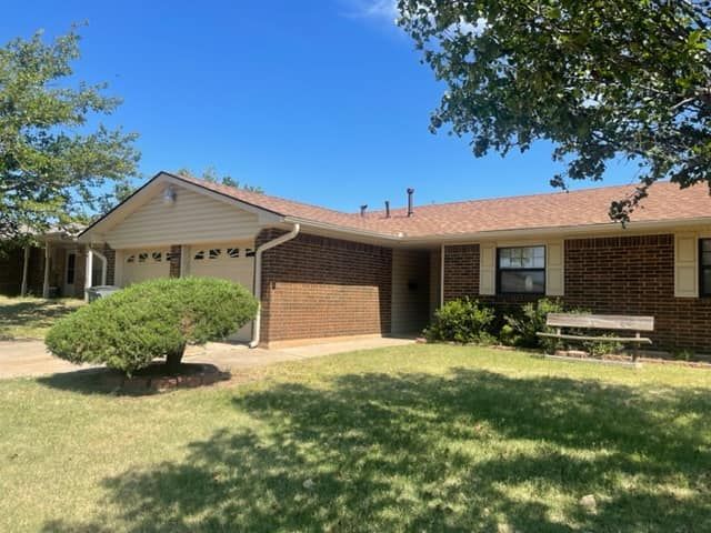 Brick and tan duplex with attached garages, brown roof, green lawn, and a clear blue sky.