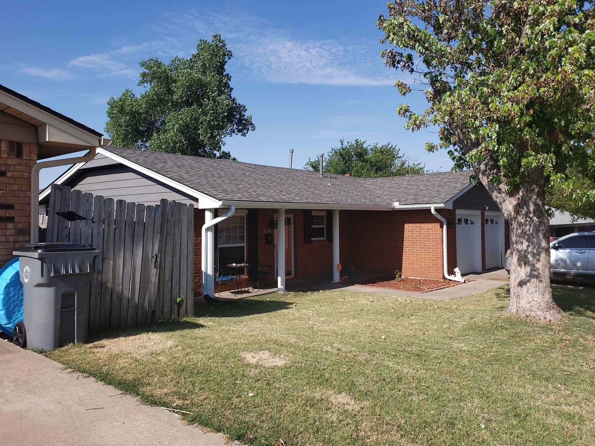 Brick house with a gray roof, wooden fence, and two-car garage under a blue sky.