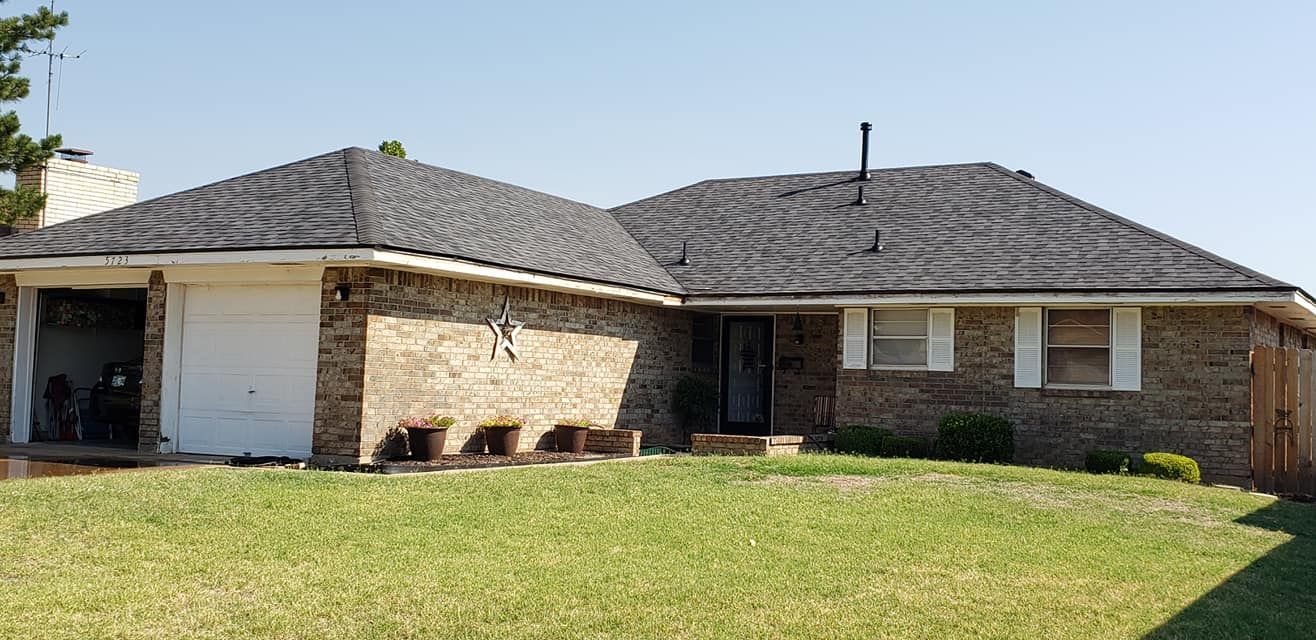 A one-story brick house with a garage, green lawn, and blue sky.