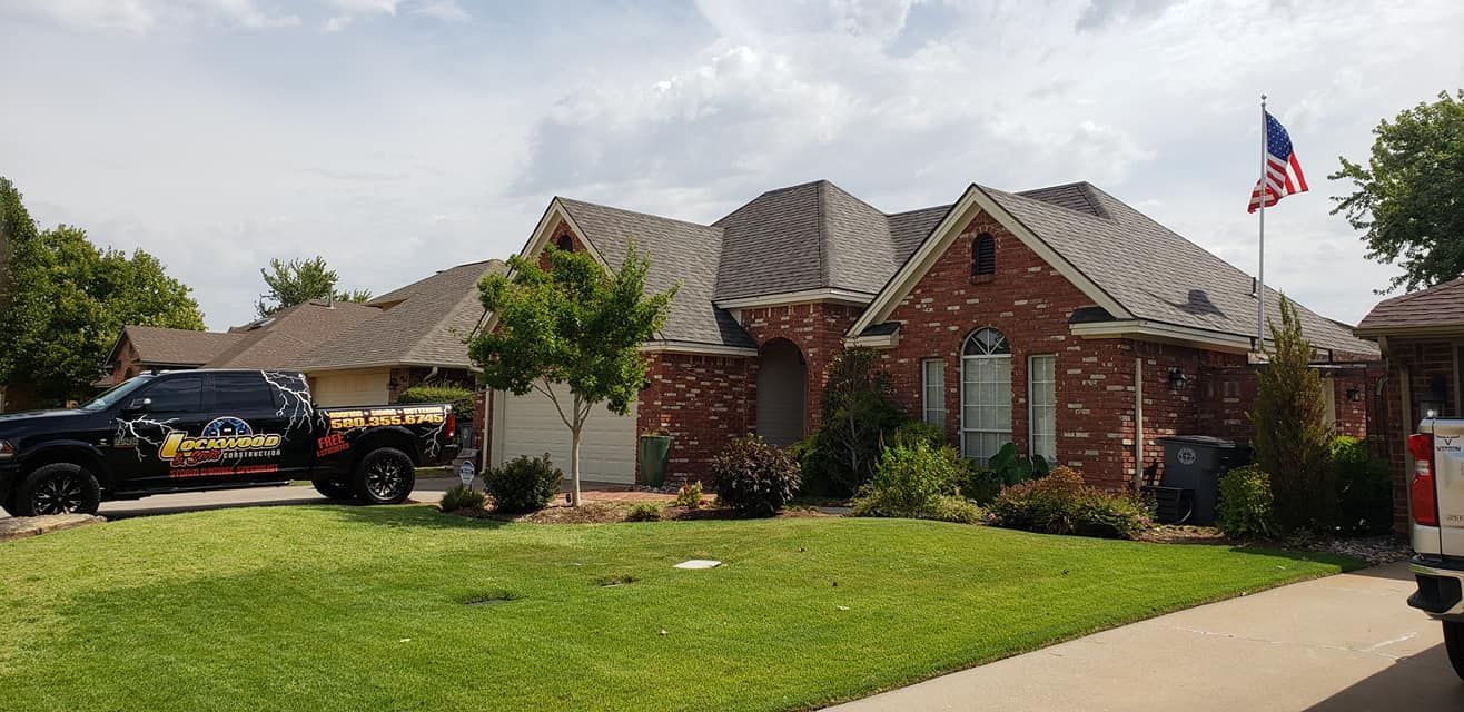 A brick house with a green lawn and an American flag waving in the sky. A truck is parked on the property.
