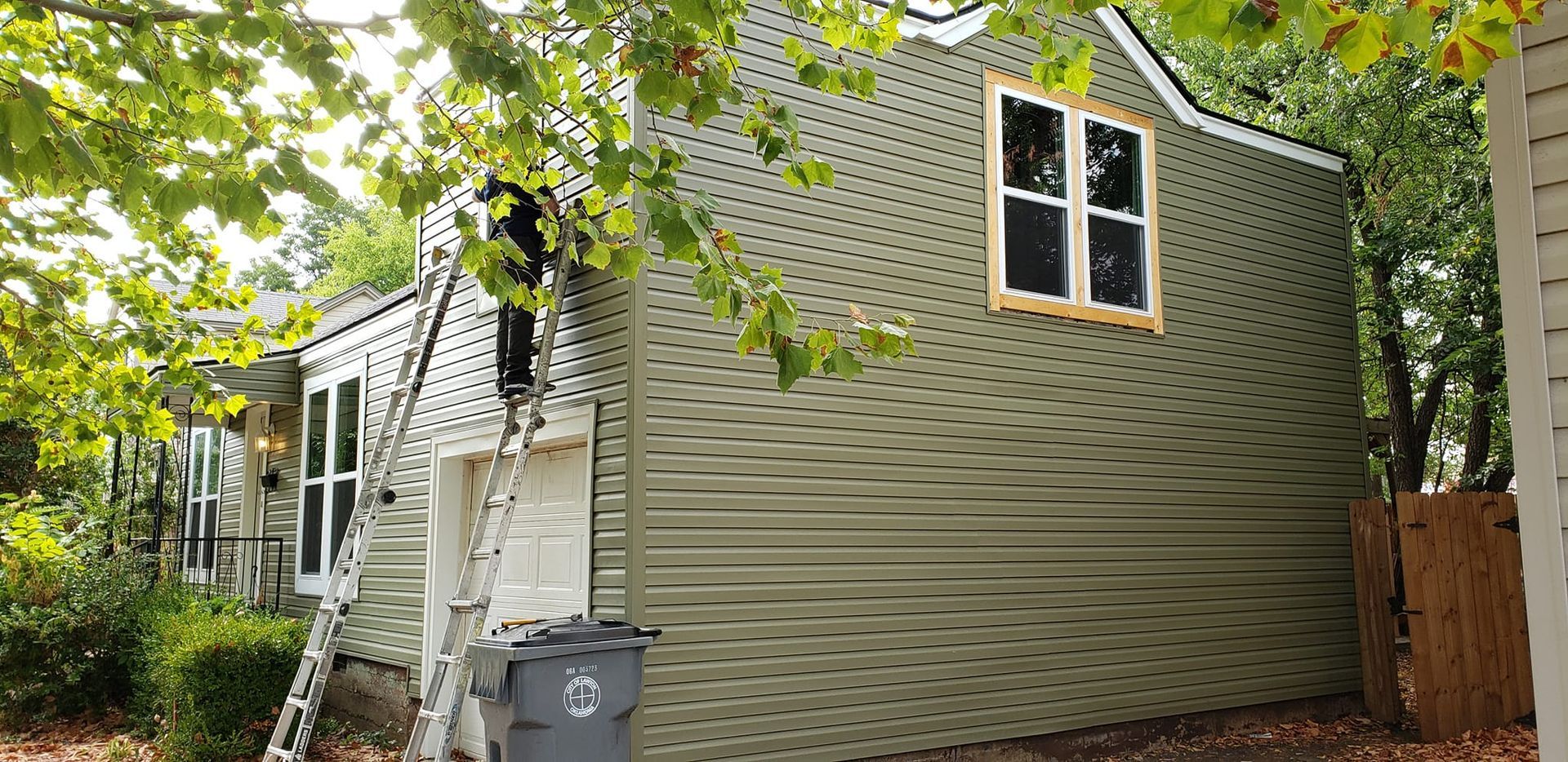 A light green building with diamond-shaped siding, window, and ladder, with trees in the foreground.