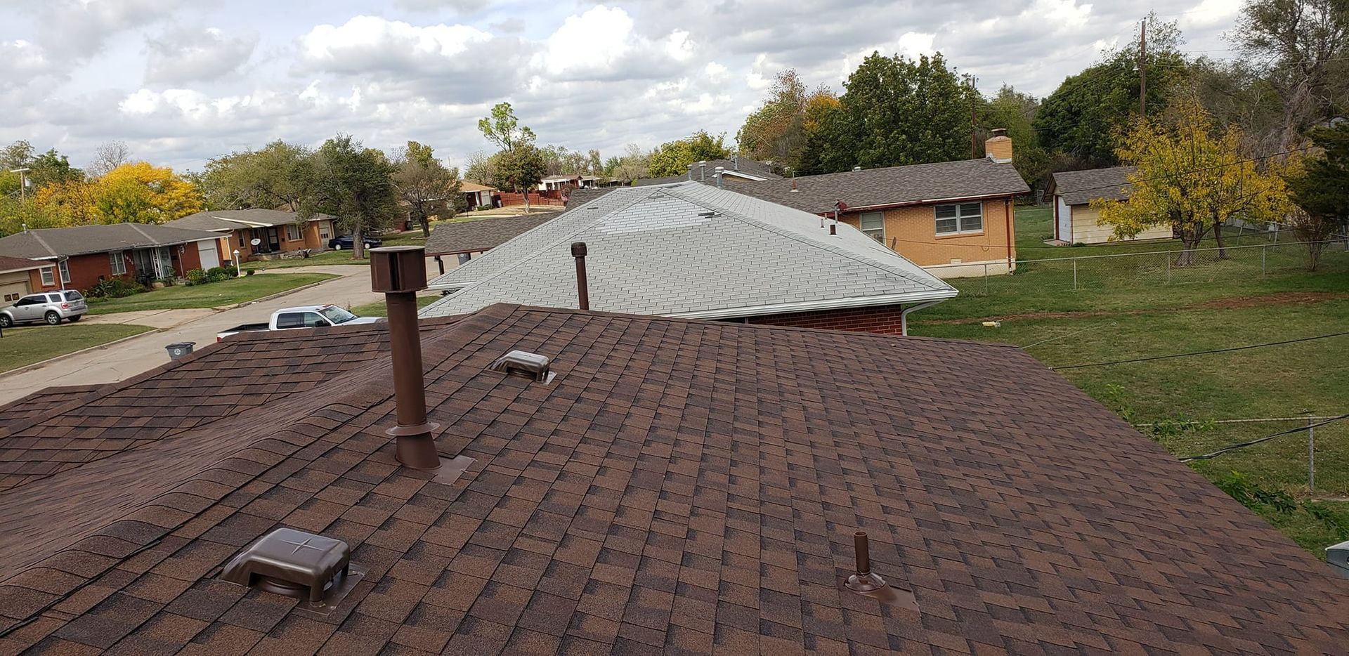 View of rooftops of houses in a suburban setting, trees in the background under a cloudy sky.