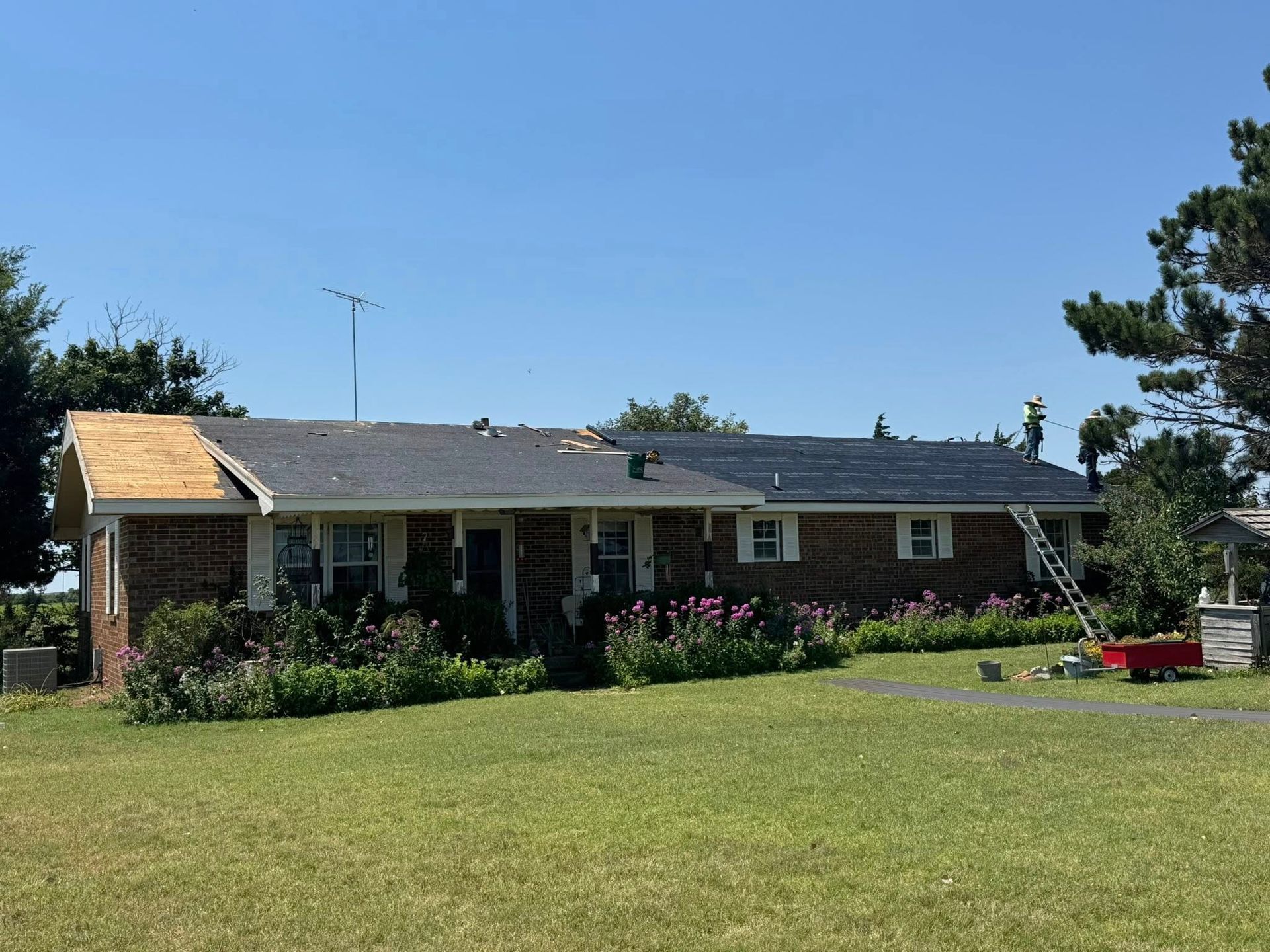 Brick house with new roof installation. Men on roof, blue sky.