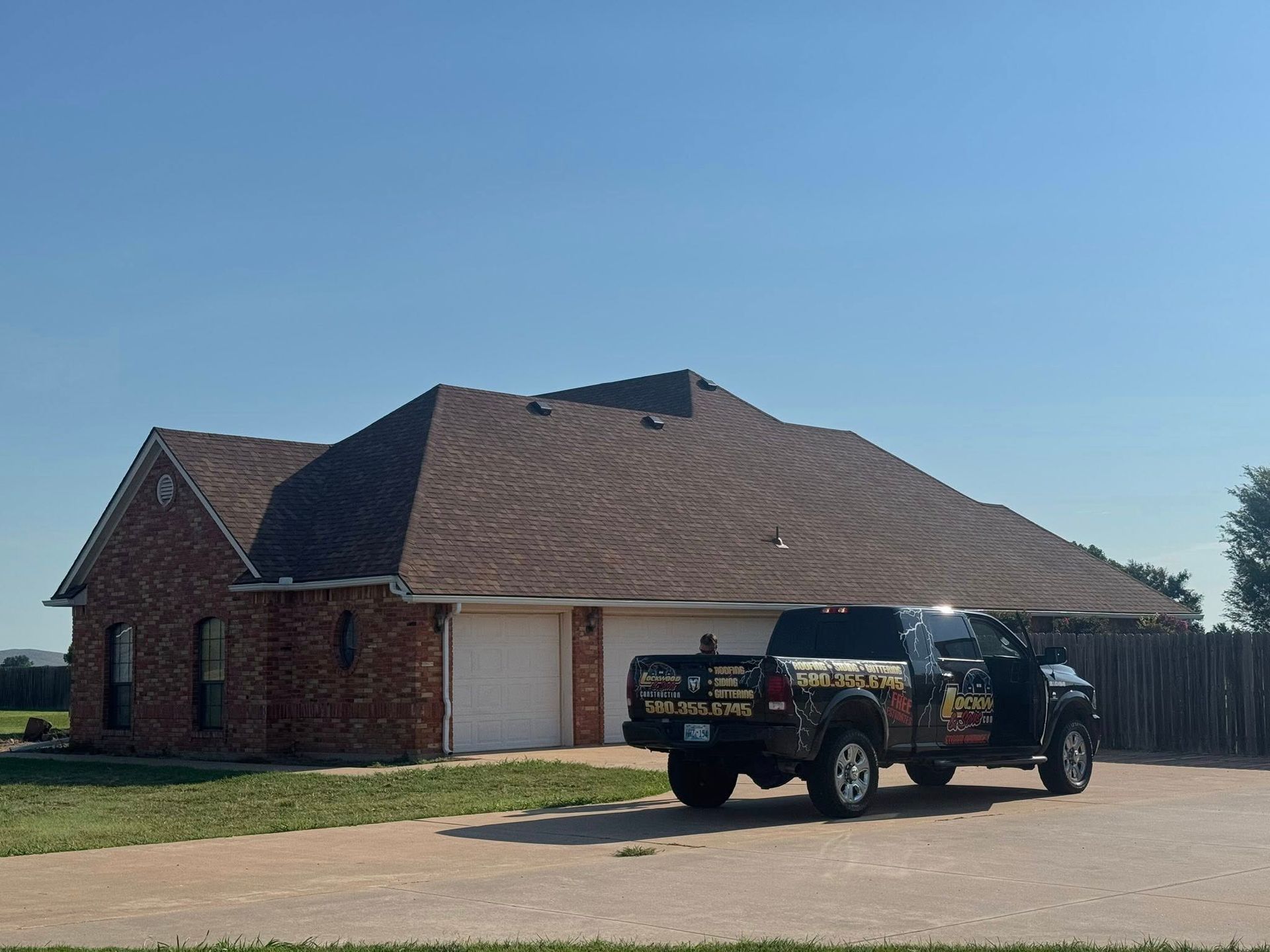 Black truck parked in front of a brick house with a new brown roof under a blue sky.