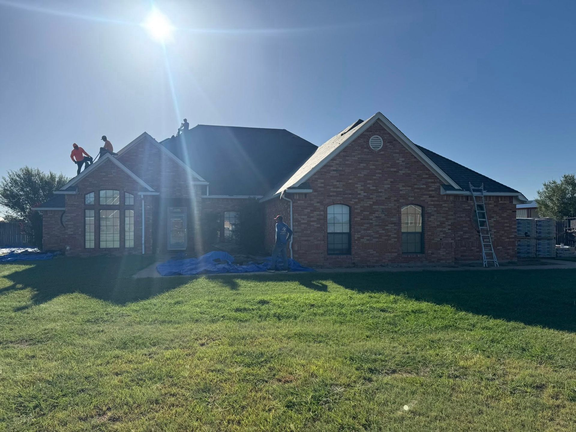 Roofers on a brick house with dark shingles; sunny day.