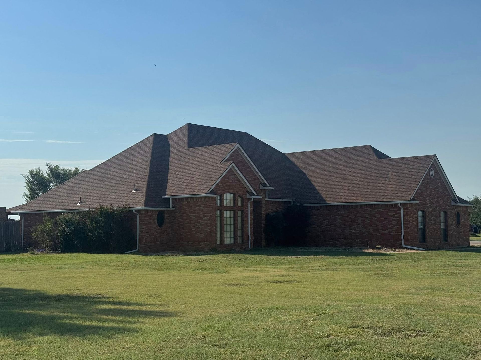 Brick house with brown roof on a green lawn under a blue sky.