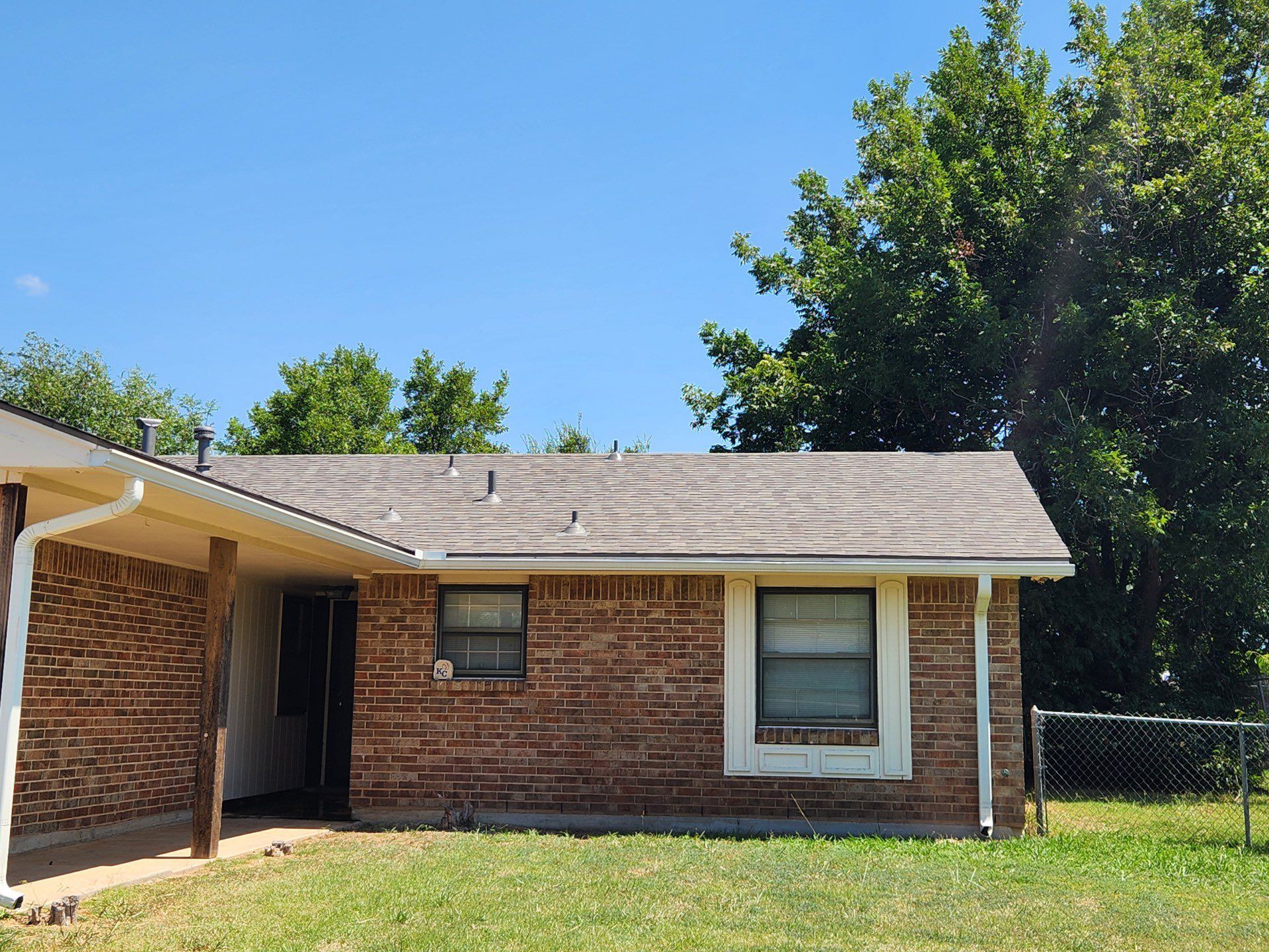 Brick house with a brown roof, two windows, a covered porch, and a grassy lawn. Clear, blue sky.
