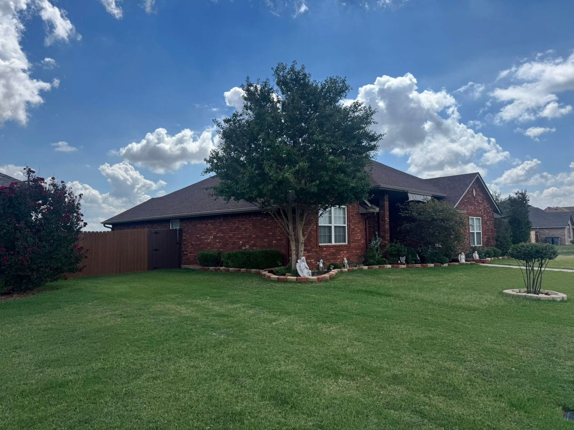 Brick house with green lawn and tree against a blue sky with clouds.