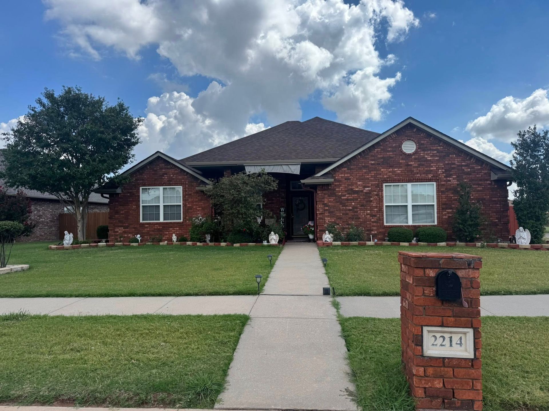 Red brick house with green lawn and cloudy sky; mailbox in the foreground.