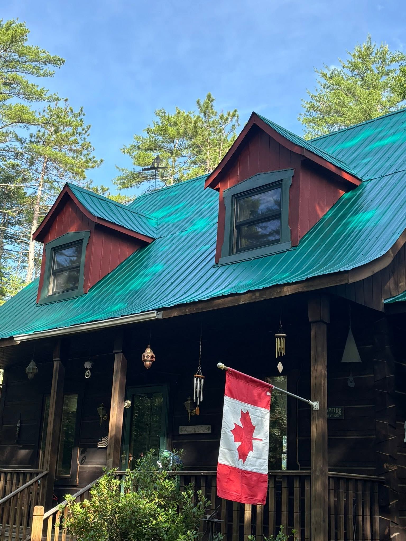 Rustic cabin with a green roof and a Canadian flag hanging by the porch.