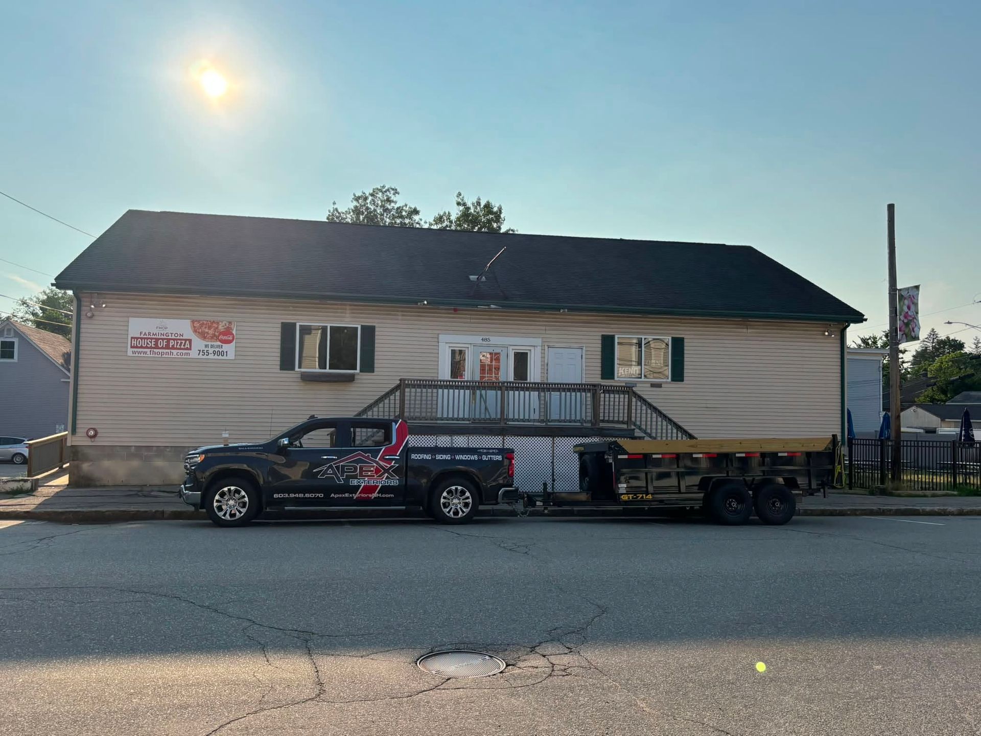 Pickup truck hauling a trailer beside a beige building on a sunny street