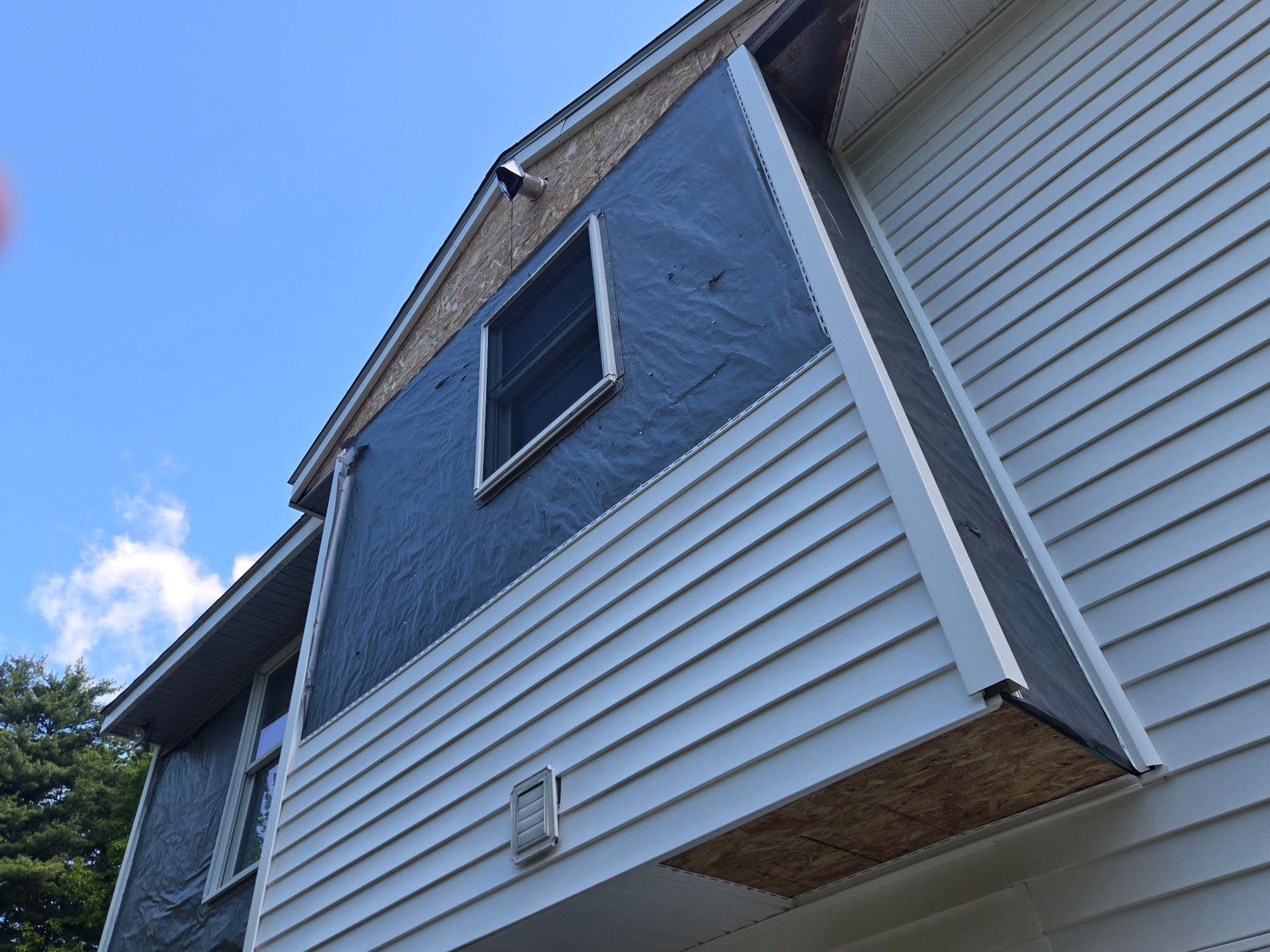 Close-up of a house exterior with blue siding, white trim, and a window against a bright sky