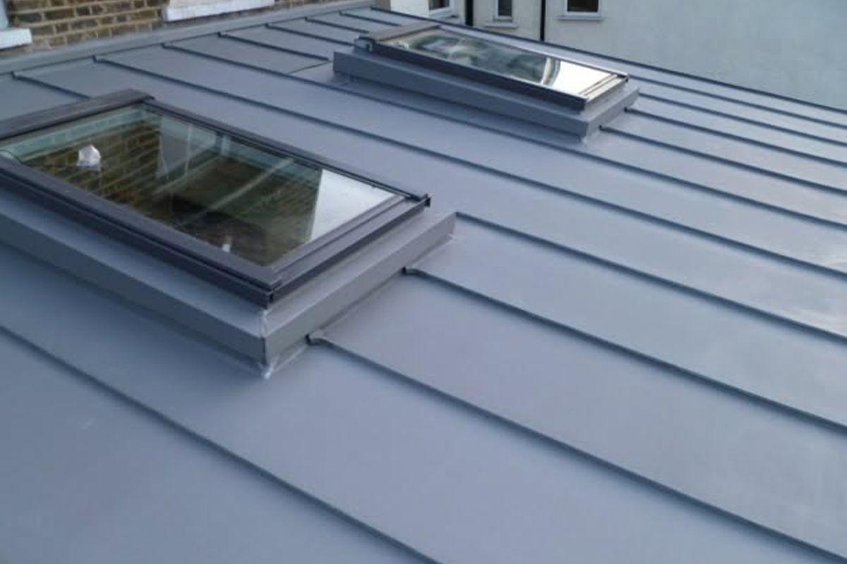 Two skylights on a gray metal roof near a brick wall