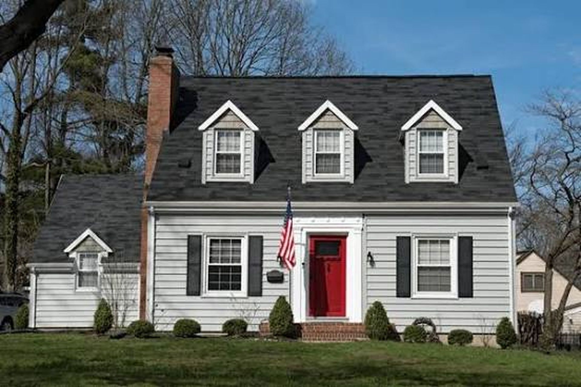 Gray two-story house with red door, white trim, and American flag in front yard.