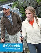 A man and a woman are walking down a trail next to a river.