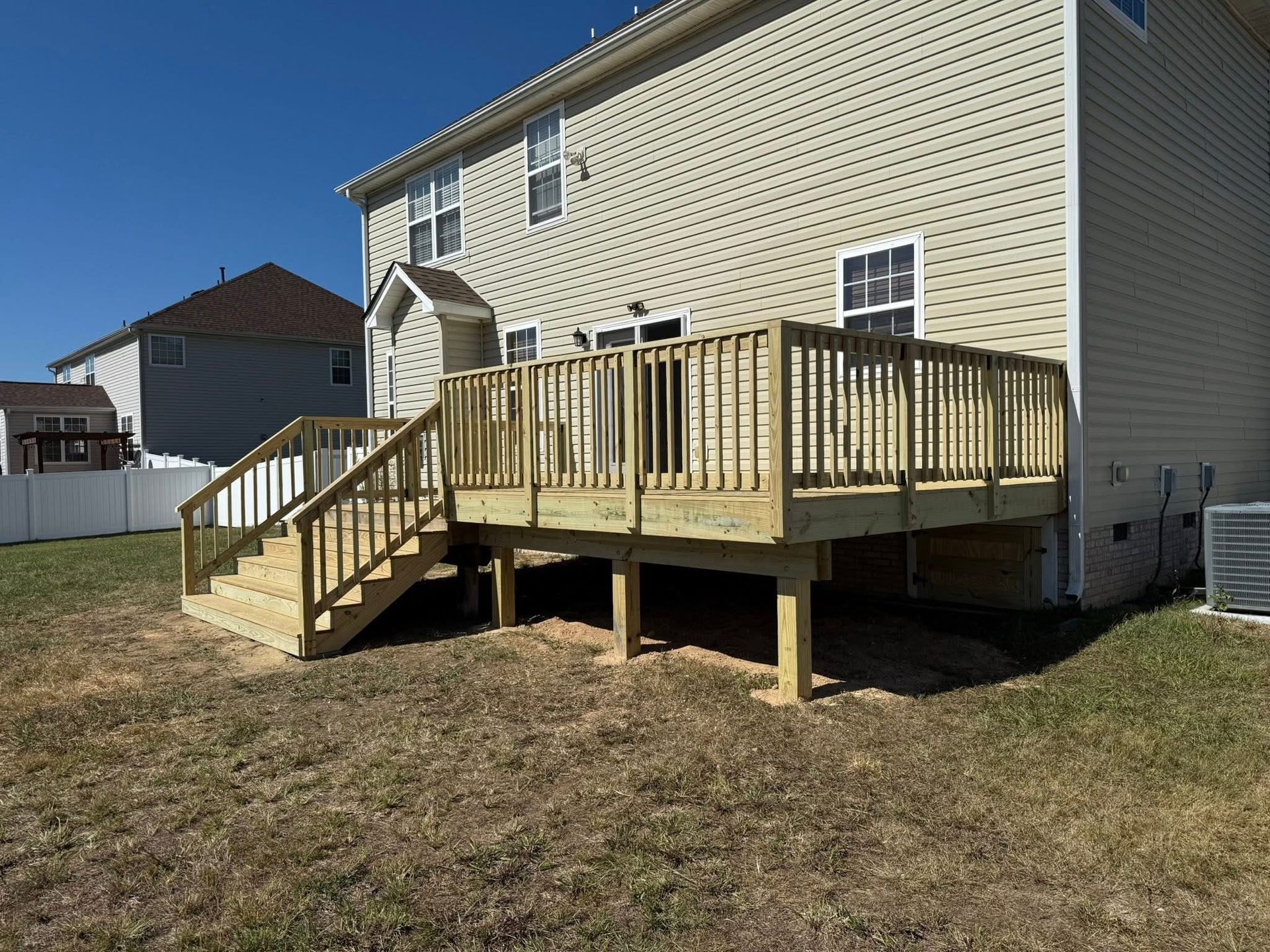 Backyard wooden deck with stairs attached to a beige house on a grassy lot