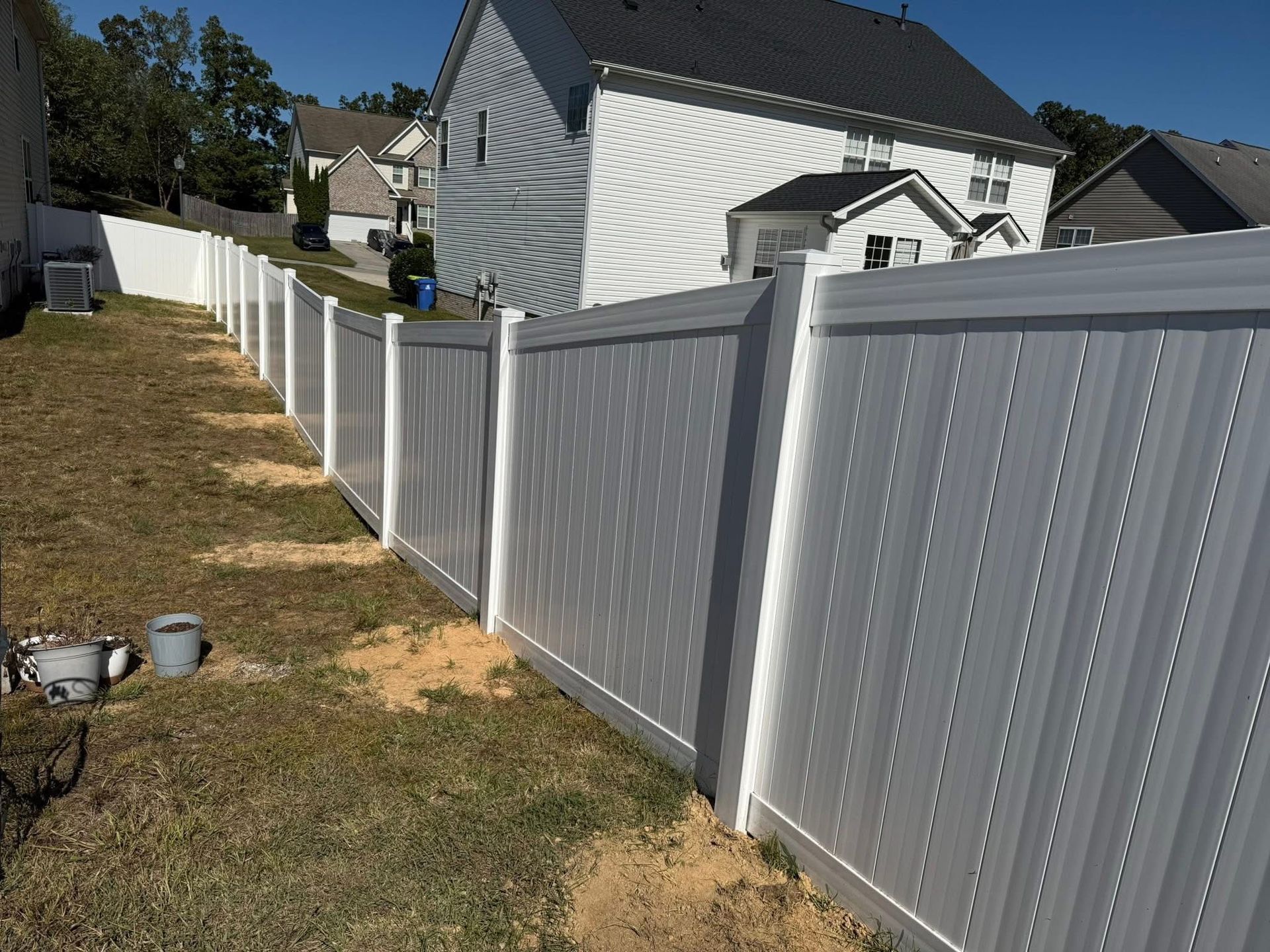 Gray vinyl fence along a grassy side yard beside houses on a sunny day