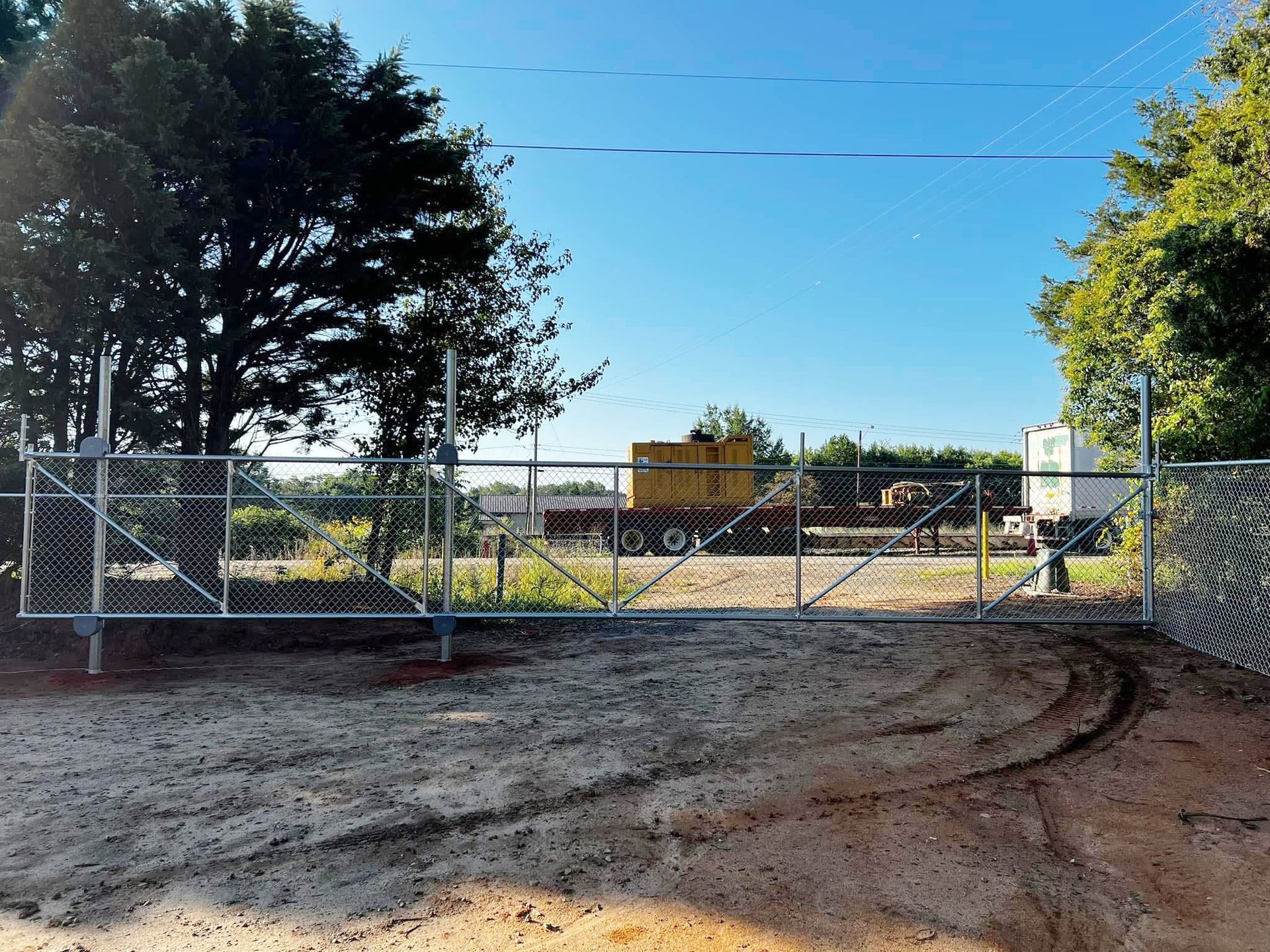 Chain-link gate across a dirt road with construction equipment behind it under a clear blue sky