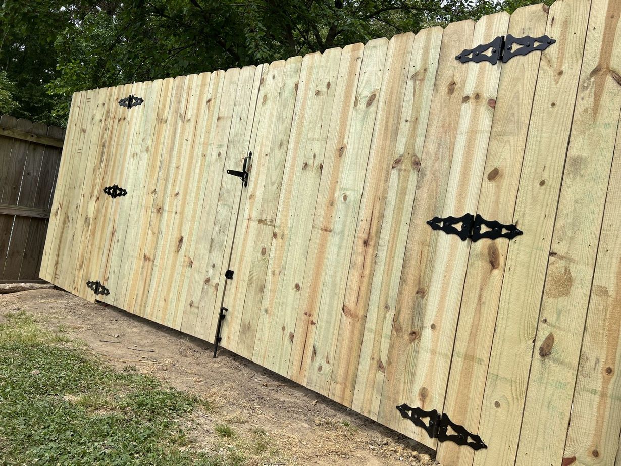 Tall beige wooden fence with black decorative hinges in a backyard, viewed at an angle.