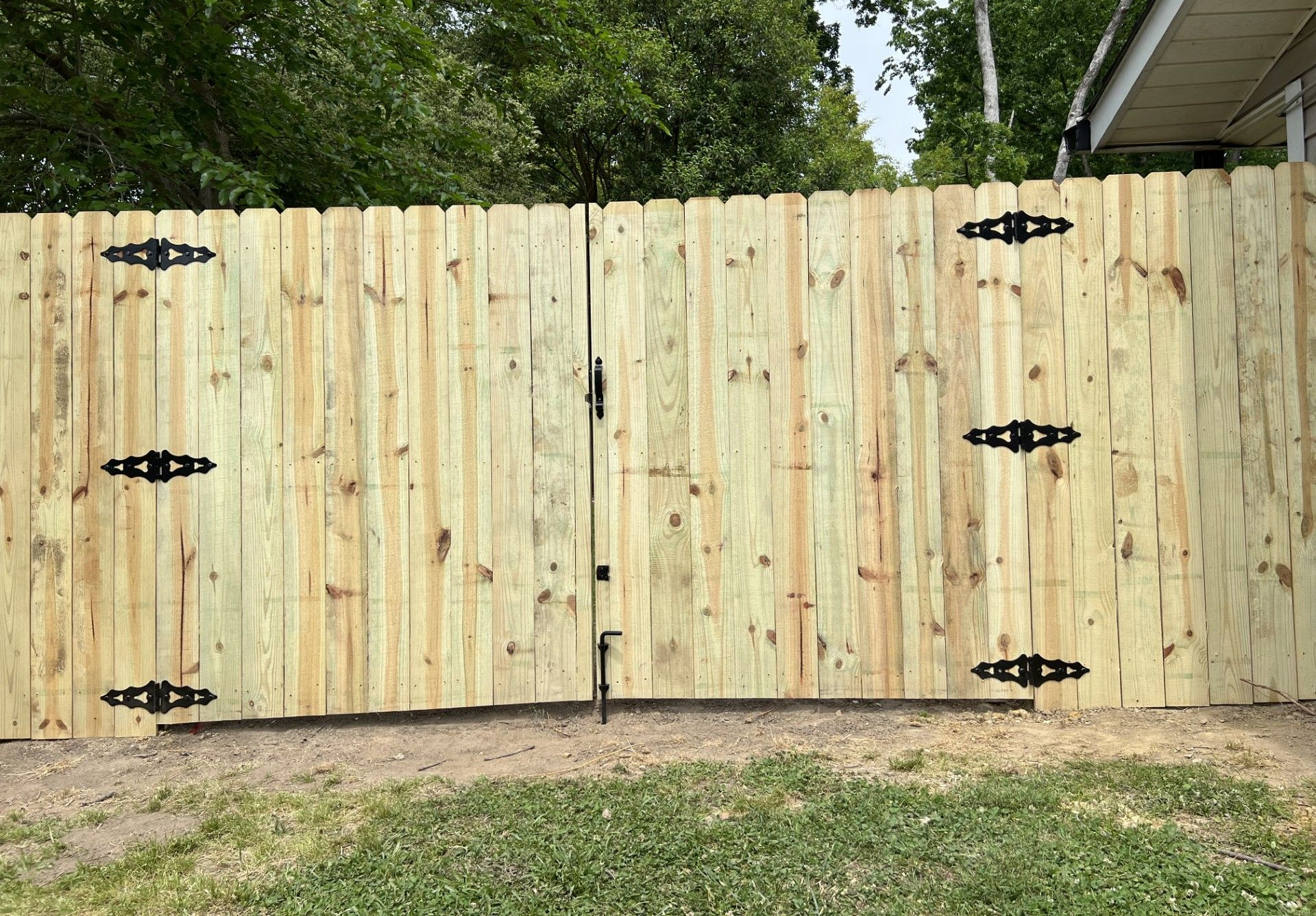 Wooden privacy fence with black hinges and a gate in a grassy yard.