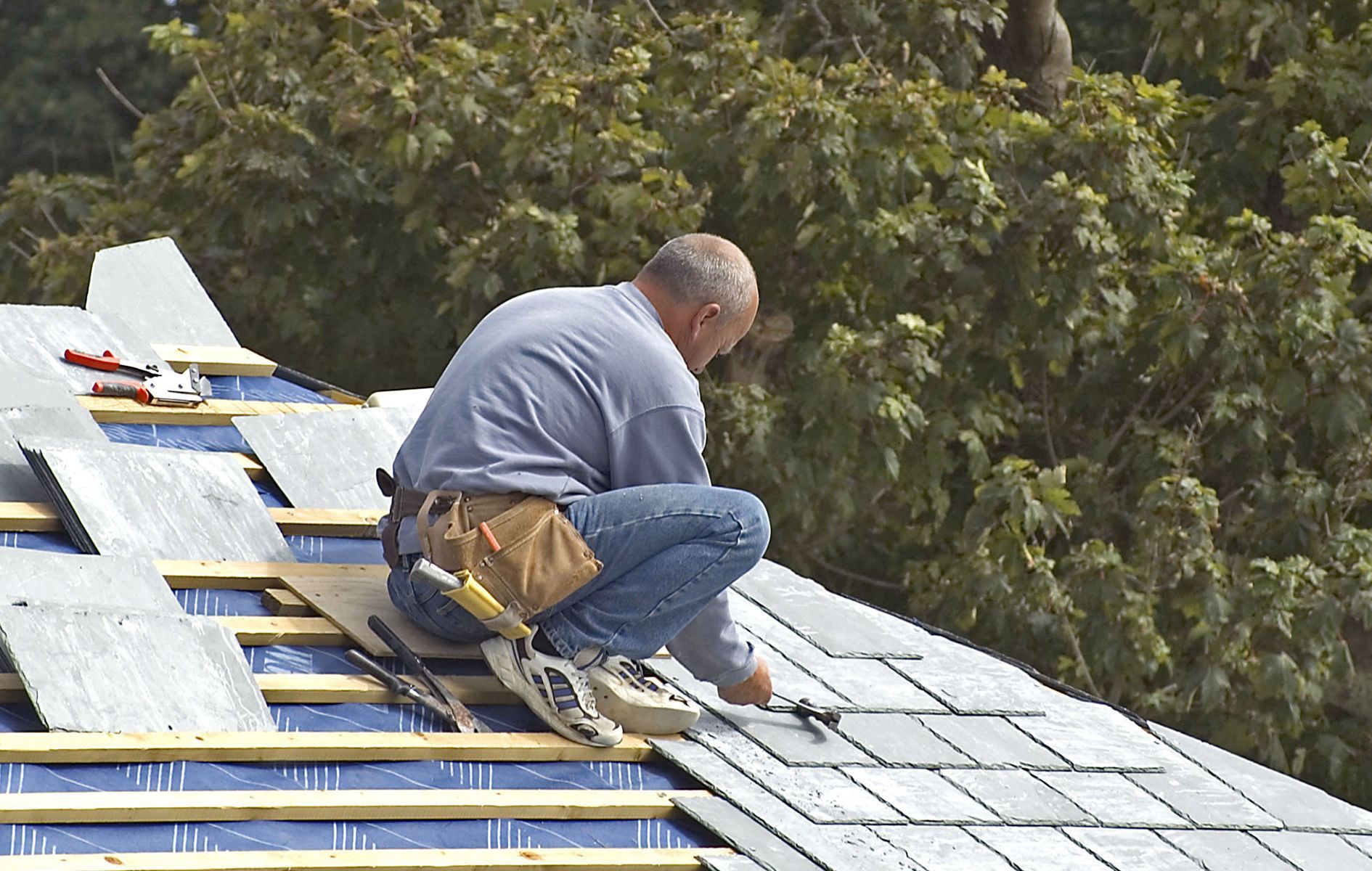 A man is kneeling on top of a roof working on it
