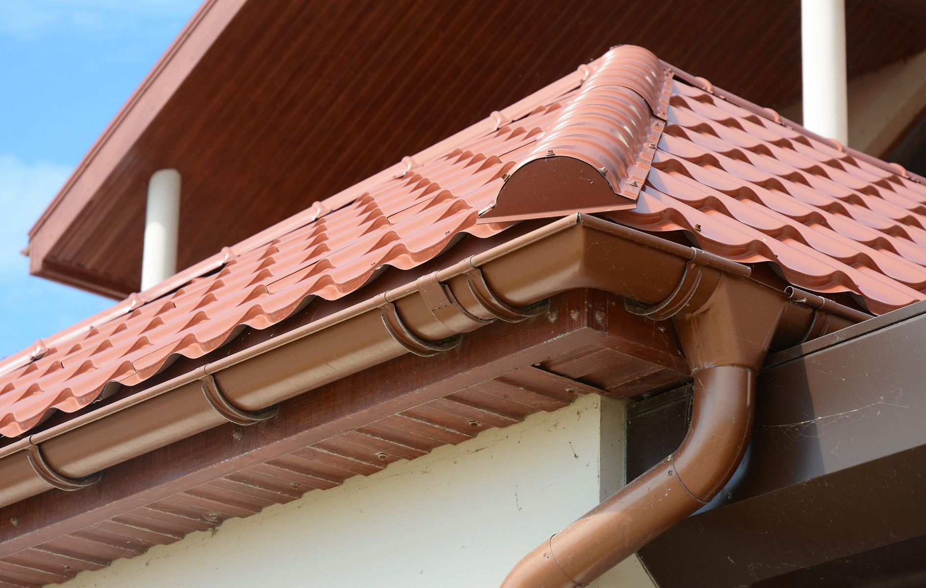 A brown gutter on the side of a house with a red tile roof