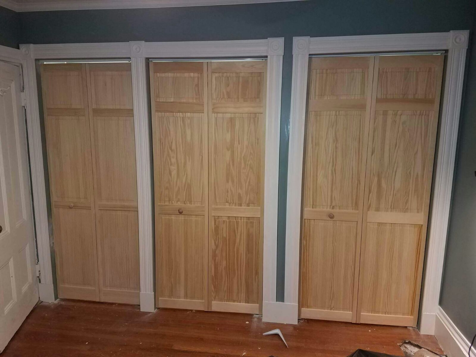 Three wooden closet doors are being installed in a room.