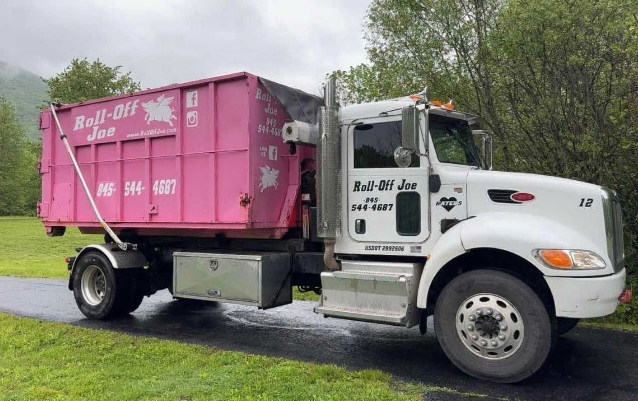 Pink dumpster truck parked on a wet road beside green grass and trees