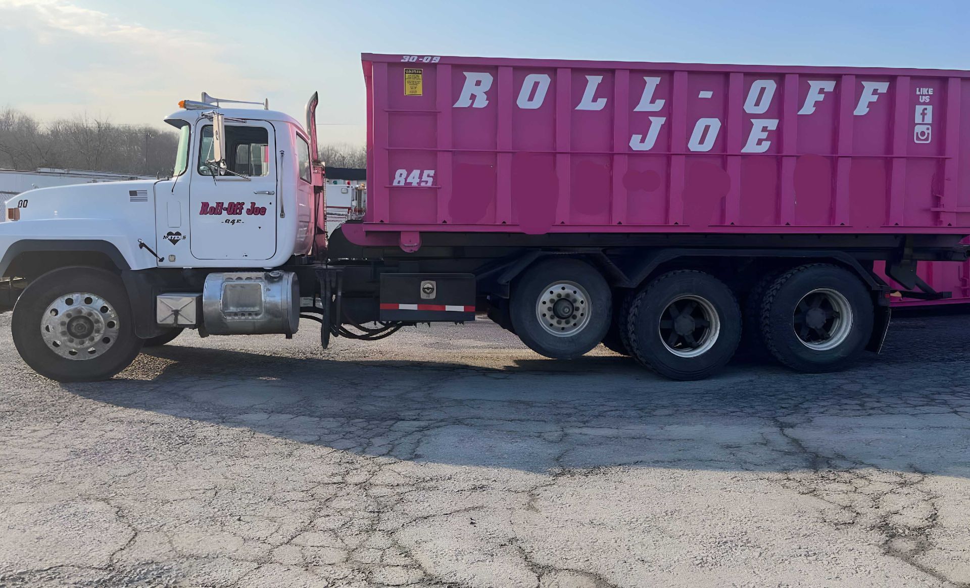 White truck hauling a pink dumpster labeled 