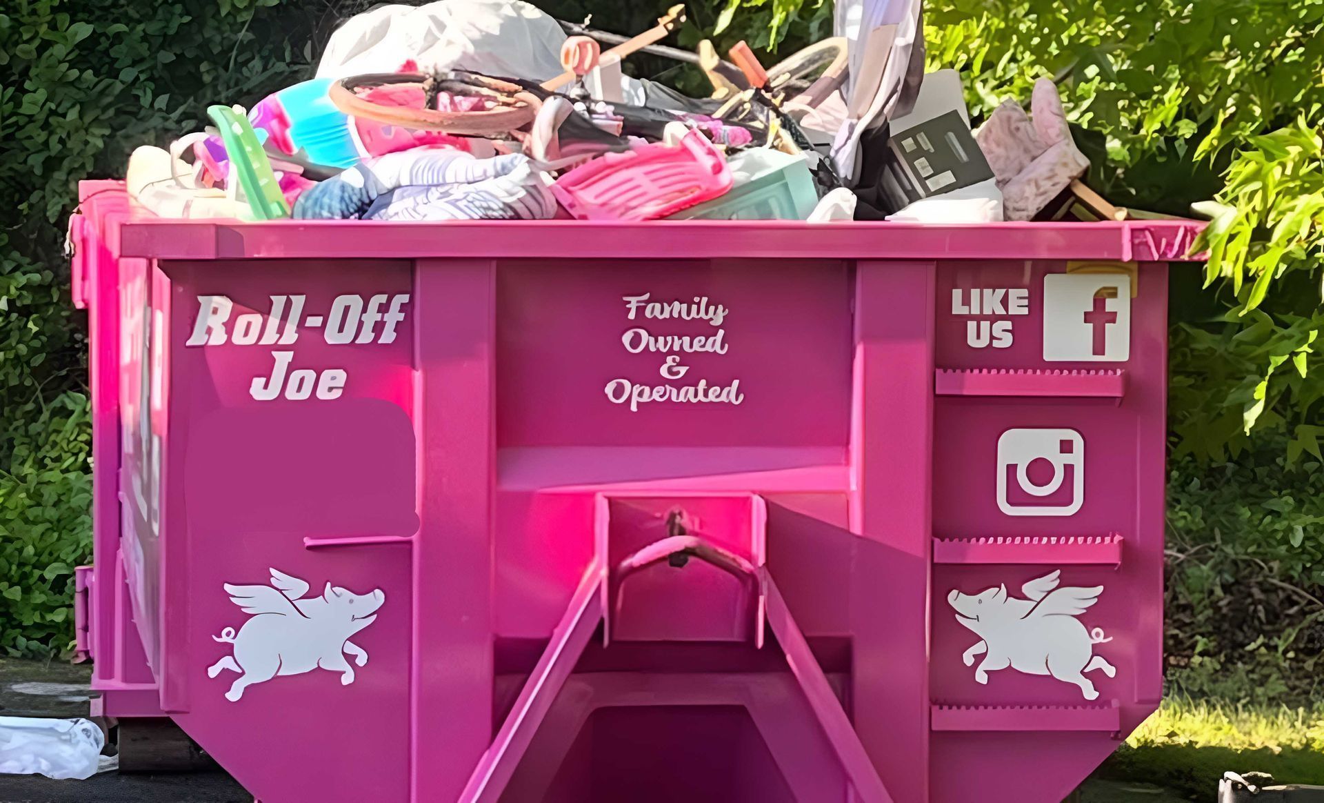 Pink graduation dumpster with Roll-off Joe and social media logos, filled with decorations.