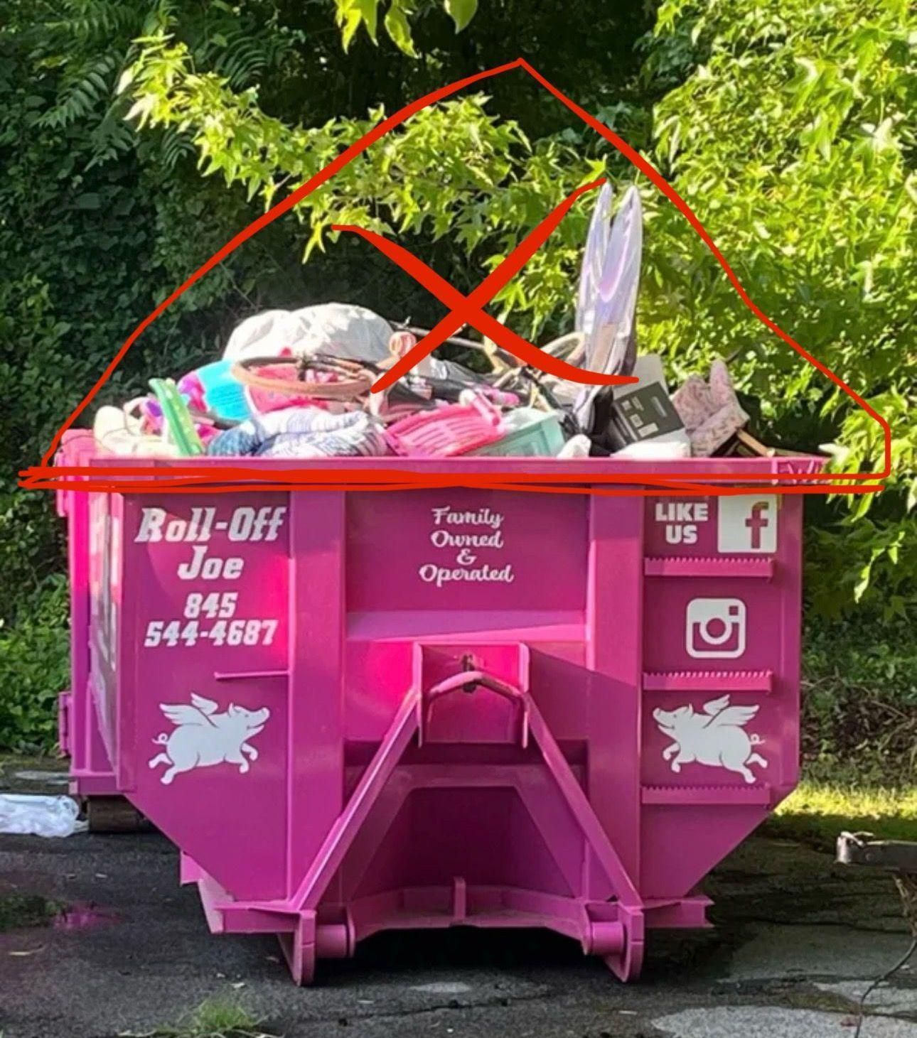 A bright pink Roll-Off Joe dumpster filled with debris and marked with a red X.
