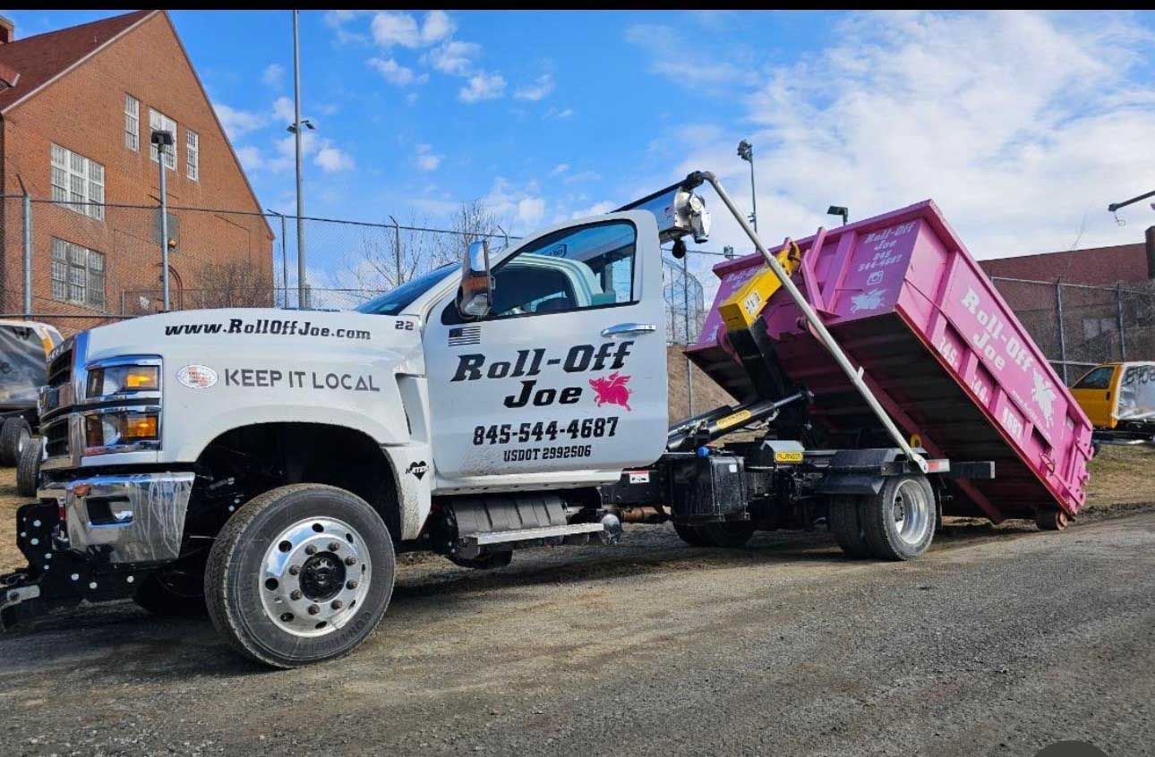 White Roll-Off Joe truck with pink dumpster, parked outdoors.