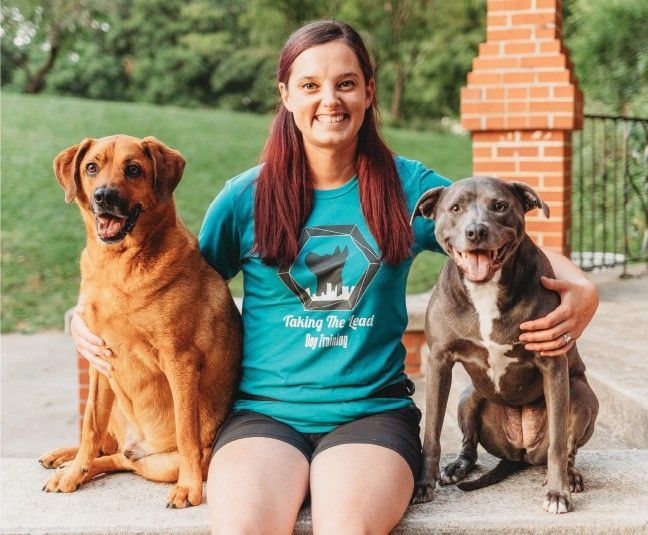 A woman in a blue shirt is sitting with two dogs