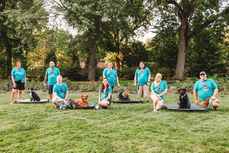 A group of people are posing for a picture with their dogs in a park.