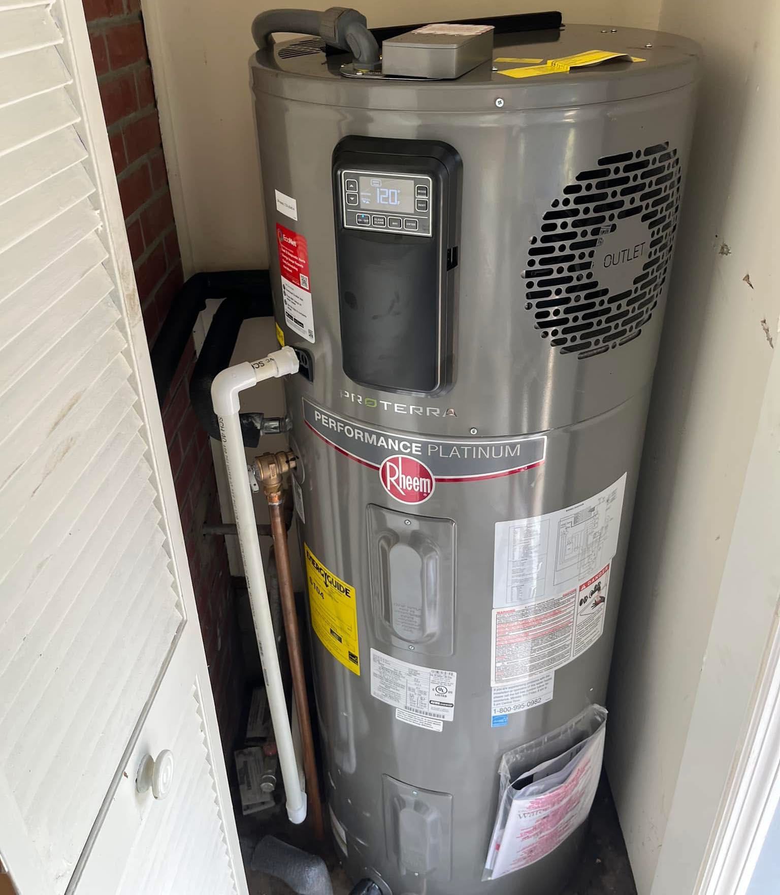 Gray water heater in a narrow utility closet with visible pipes and labels.