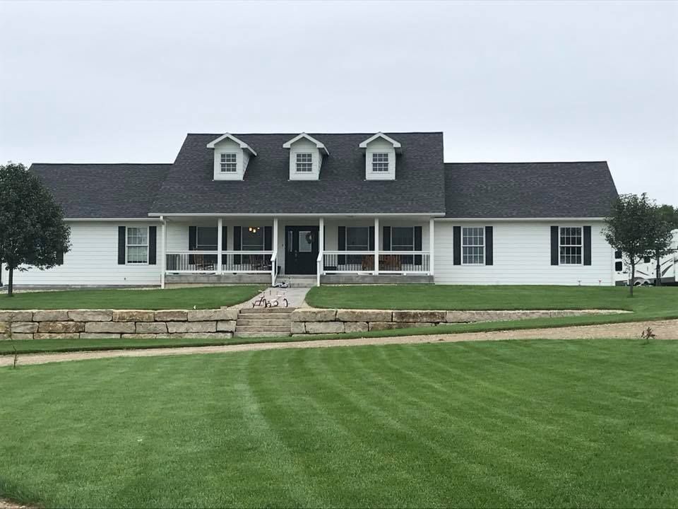 A large white house with a black roof and a large lawn in front of it.