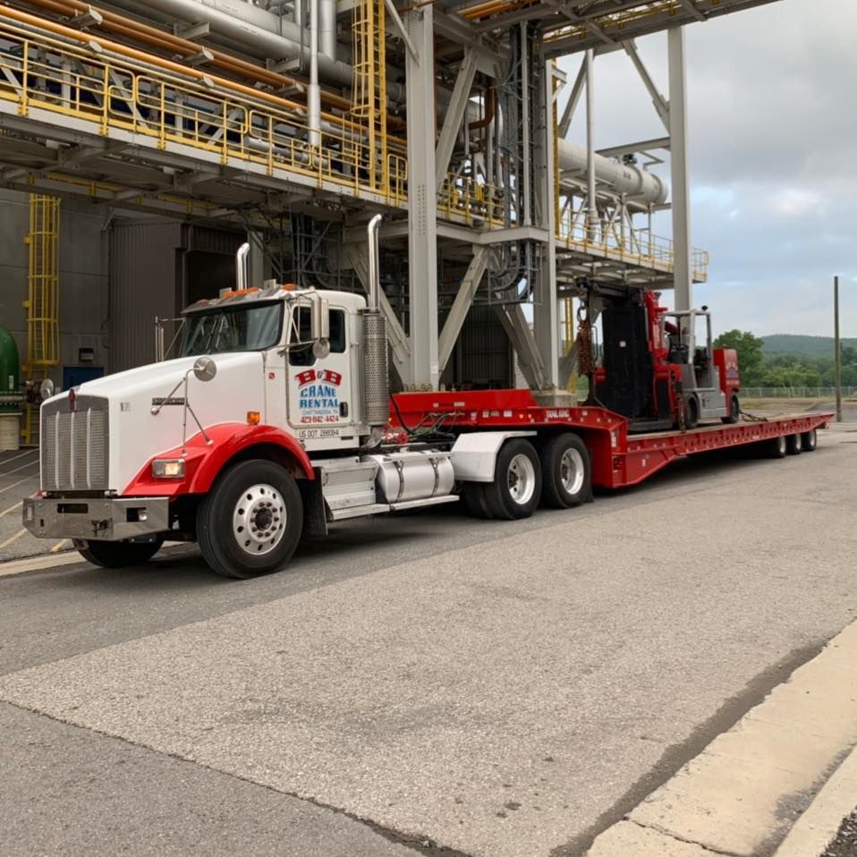 A white semi truck with a red trailer is parked in front of a building.