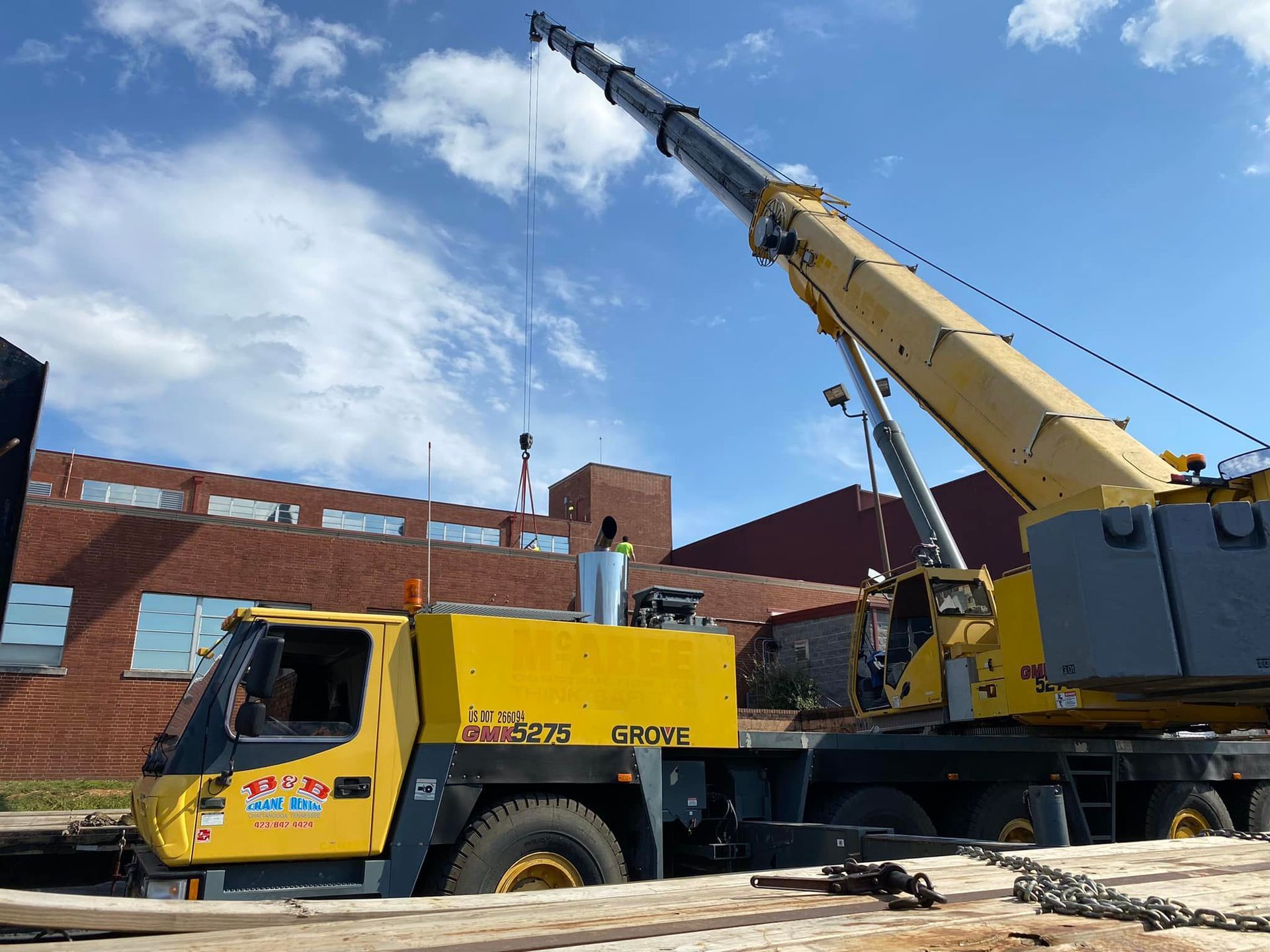 A large yellow crane is parked in front of a brick building.