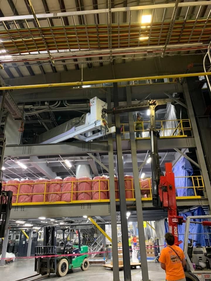 A man in an orange shirt is standing in a large industrial building.