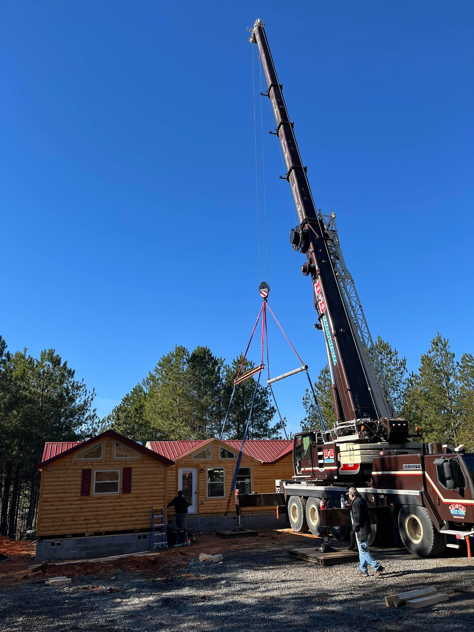 A large crane is lifting a piece of wood into a house.