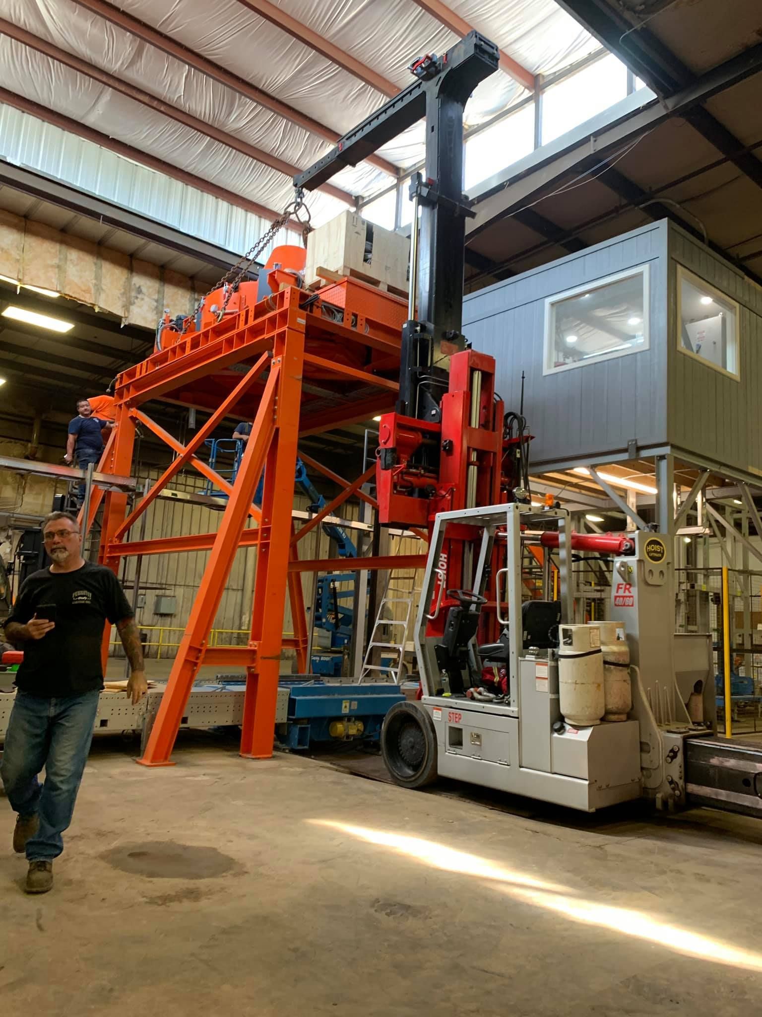 A man is walking in front of a large machine in a factory.