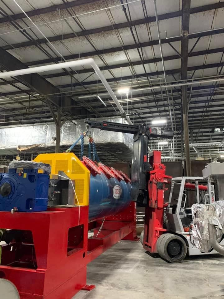 A large machine is sitting in a warehouse next to a forklift.