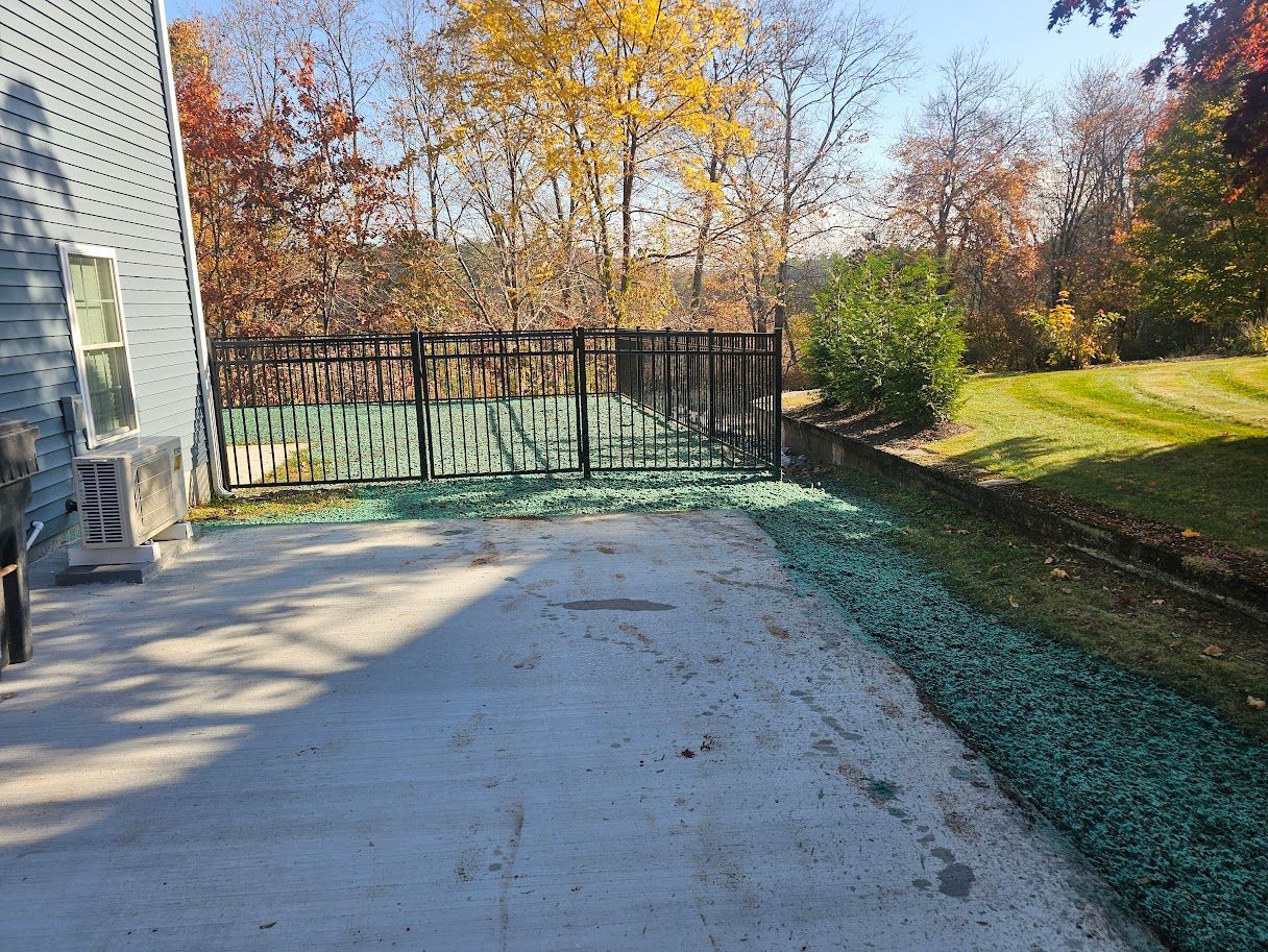 A concrete patio area adjacent to a house wall, bordered by teal decorative landscaping stones and a black metal fence