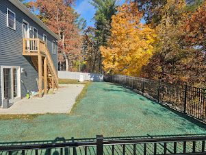 A side view of a gray house with a wooden staircase leading to a patio beside a yard covered in green erosion control mat