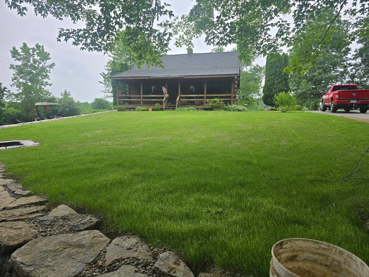 Log cabin with porch on a grassy hill; red pickup truck parked nearby; overcast sky.