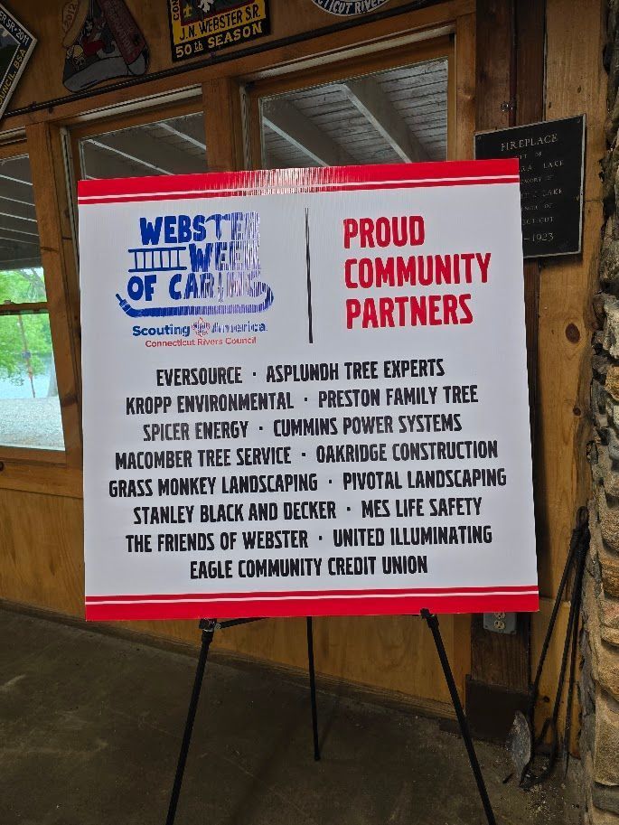 A sign listing Proud Community Partners for Webster, including Eversource, Stanley Black and Decker, and other organizations.