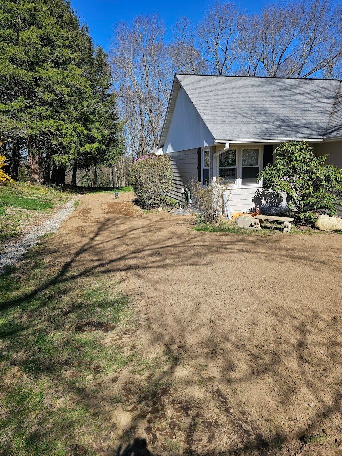 A house with a cleared dirt patch in the front yard, a path, and trees on a sunny day.