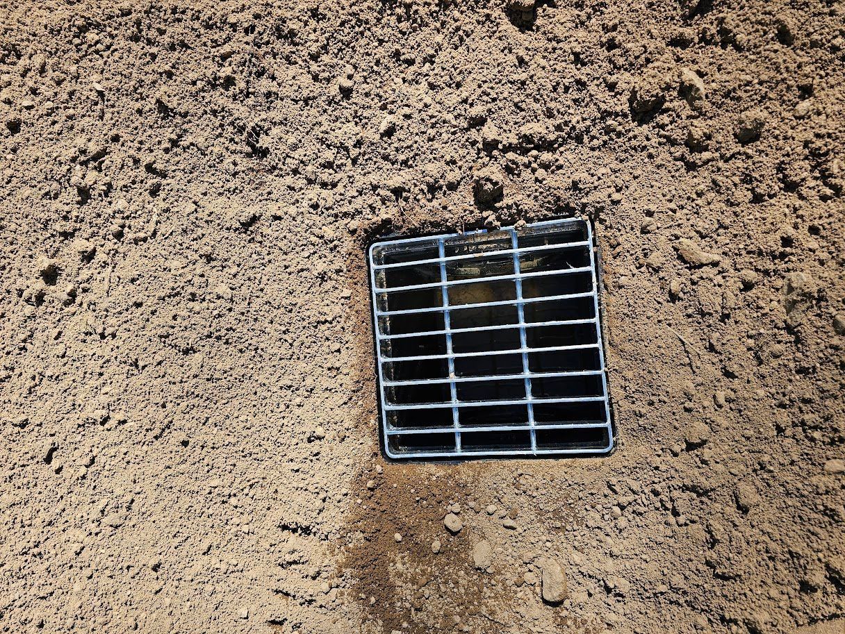 Square metal drain in dirt.